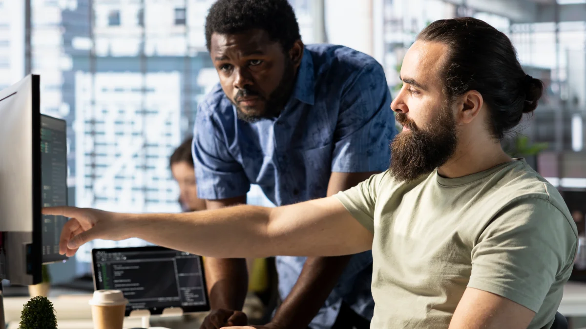Male employees looking at computer screens and pointing